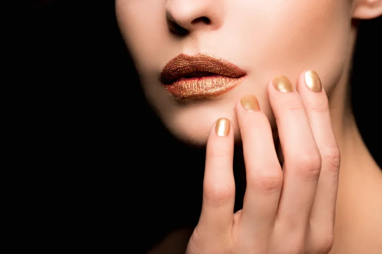 Cropped image of a woman with makeup and a golden nail art.
